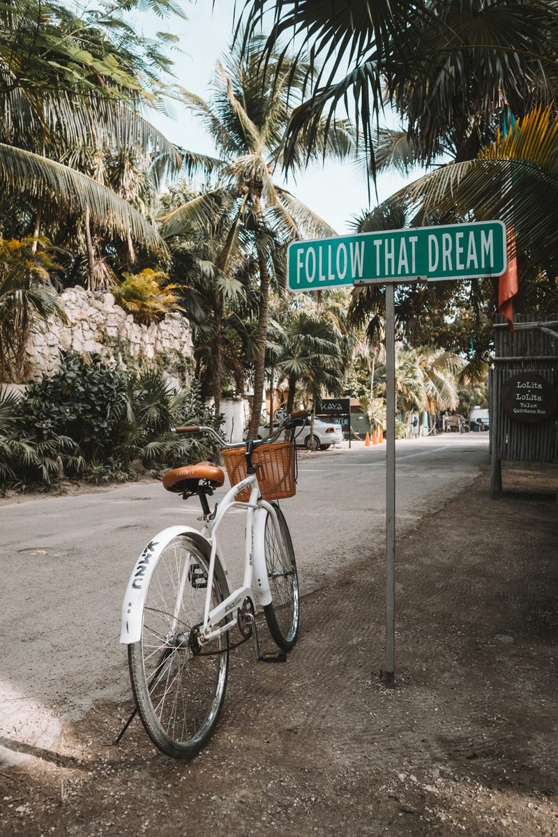 Bicycle next to a 'Follow That Dream' street sign in a tropical setting