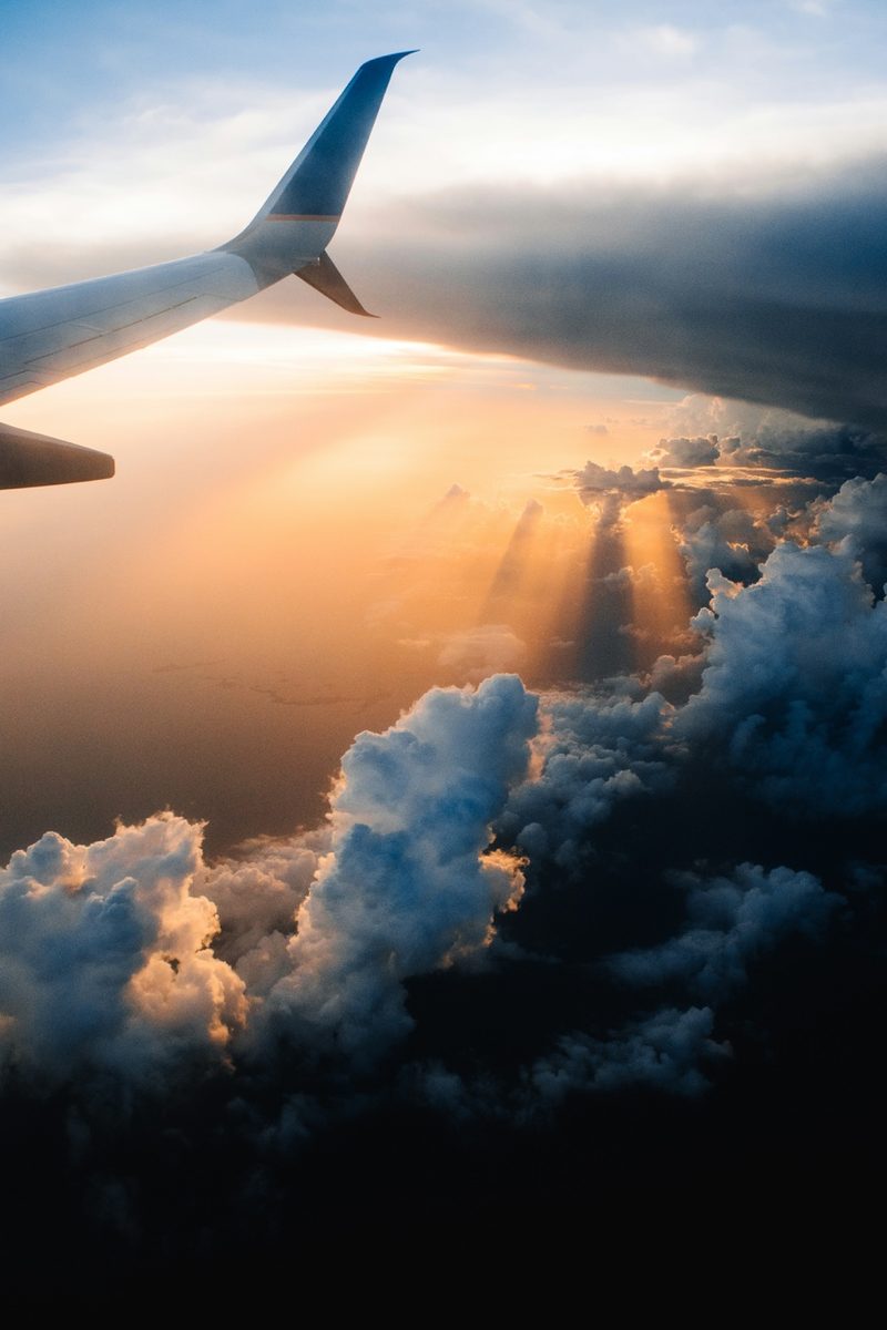 Aircraft wing breaking through golden sunrays above the clouds